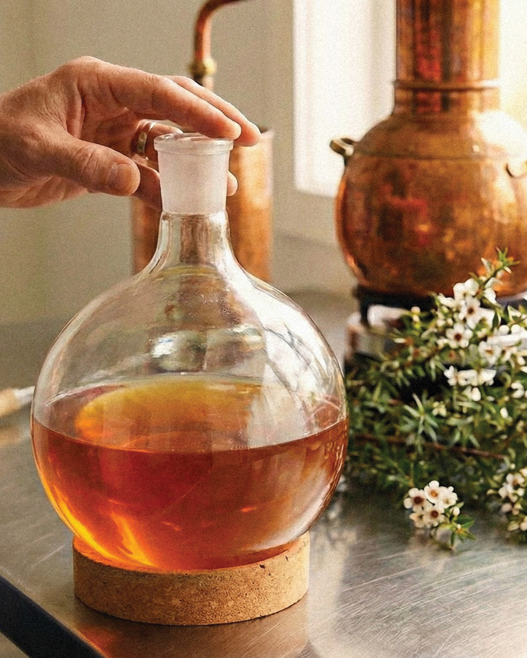 Glass decanter with liquid on a metal surface, with a hand holding the stopper.